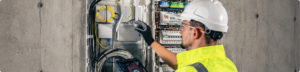 Électricien portant des EPI intervenant sur une armoire électrique pour une opération de maintenance. - Securinorme